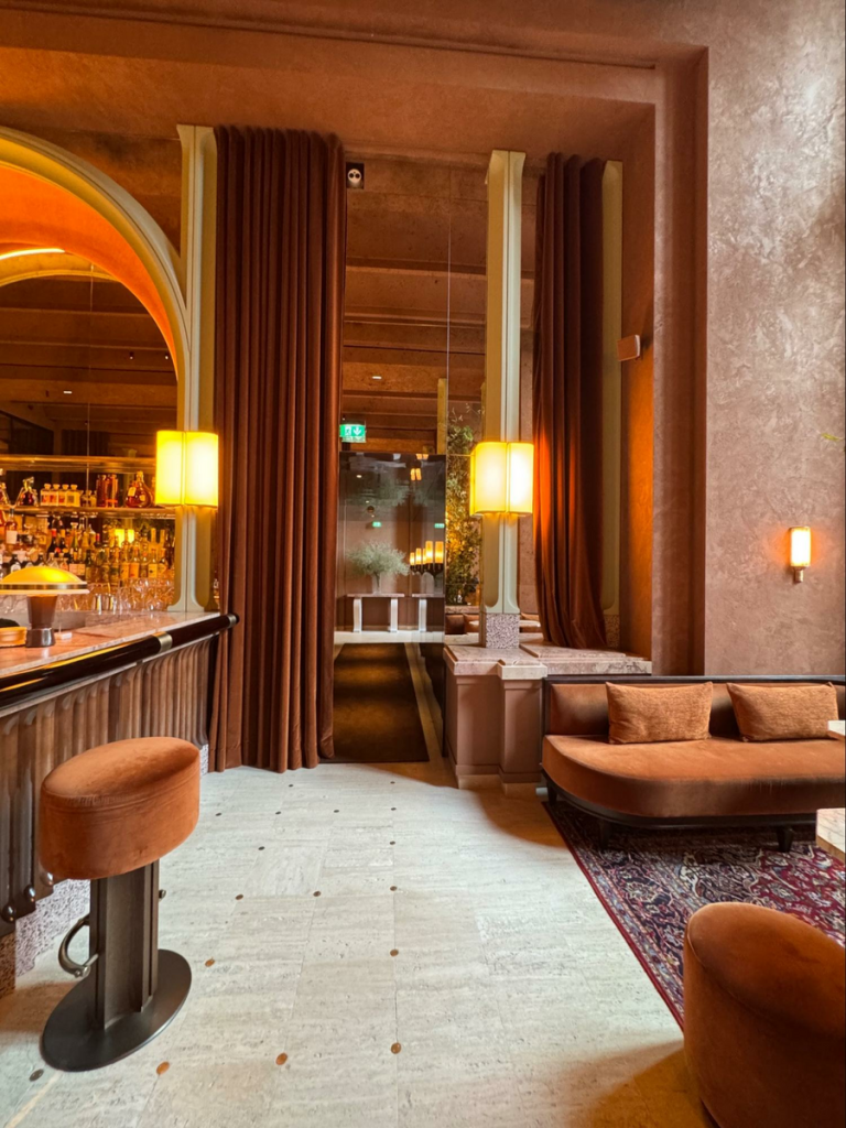Wood Highlights: Lacquered wall treatment in the hall beyond and curved moulding at the bar leads the way to this narrow passage, gently and almost ceremoniously guiding visitors with its luminous and reflective surface.