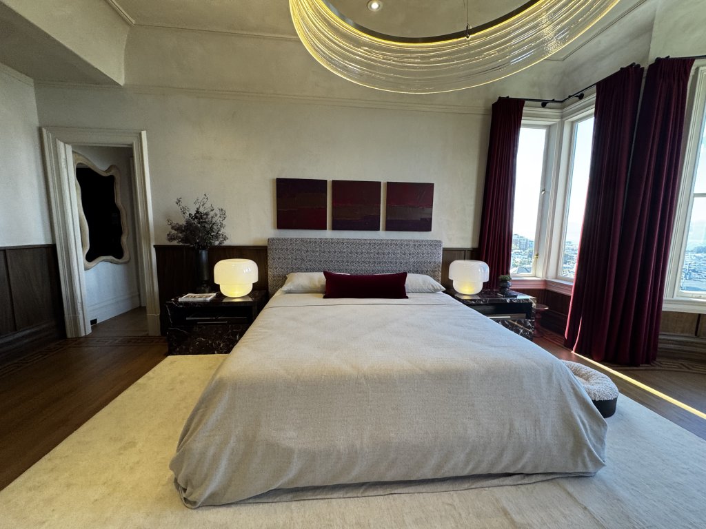 Wood Highlights: The primary bedroom, “West | Red Bedroom” by Castellanos Interiors, at the 2026 San Francisco Decorator Showcase, the 1897 Queen Anne Victorian at 2315 Broadway designed by architect Moses J. Lyon. Deep casings frame the interior door and the coveted, view-facing bay window, a defining feature of the city's Victorian and Edwardian interiors.